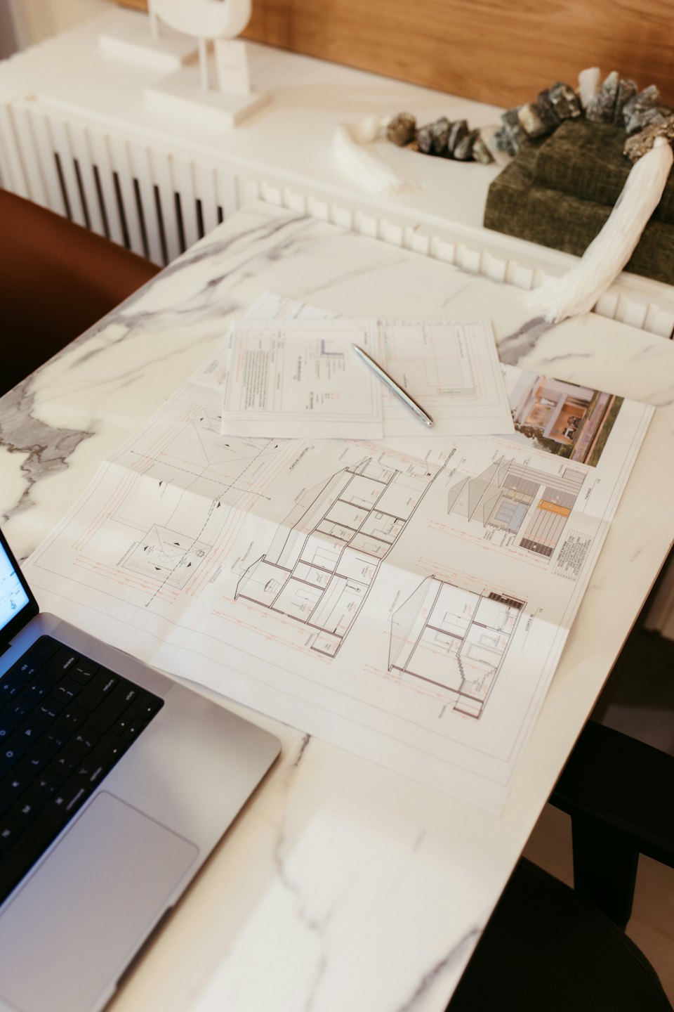 Architectural blueprints and laptop on a marble table.